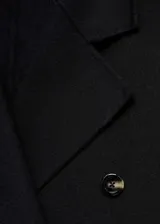 Abrigo largo negro de doble botonadura con cuello de solapa, hombros caídos y bolsillos laterales.