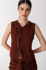 Top sin mangas color ladrillo, tejido en punto arroz con textura suave. Presenta un corte recto y lazos finitos decorativos en el frente, simulando una abertura.