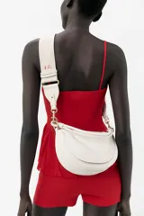 Bolso de hombro ovalado color crema con asa de doble tira redonda con detalles metalizados dorados. Incluye cierre imantado, asa de bandolera extraíble con tejido a contraste y bolso interior con cierre mediante cremallera metálica.