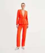 Conjunto sastrero color naranja, compuesto por un blazer entallado con solapas de muesca, cierre con lazo y pantalón de vestir recto de tiro alto.