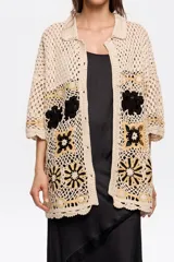 Cárdigan de algodón crochet color crema, con cuello camisero, manga corta y cierre frontal con botones. Presenta apliques de flores tejidas en negro y dorado. Corte oversize.