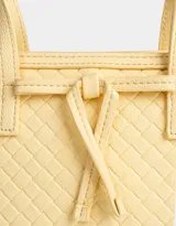 Cartera mini city color amarillo claro, de cuerina trenzada, con doble asa corta de mano, correa regulable desmontable, cierre superior y moño decorativo.