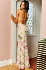 Vestido largo de fiesta color crema con estampado floral en tonos rosa y verde. Tiene escote en V, breteles finos, espalda descubierta y abertura lateral en la pierna.
