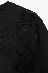 Camiseta negra de cuello redondo y manga corta con detalle de flores en relieve en el hombro.