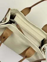 Bolso tote color crema con detalles en cuero marrón. Tiene doble asa de mano y correa de hombro extraíble con el logo de la marca.