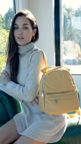 Mochila color mostaza de símil cuero con bolsillo frontal con cierre y broche, apertura superior con cierres metálicos, bolsillos laterales y asa de mano. Incluye bolsillos internos y correas regulables para colgar en la espalda.