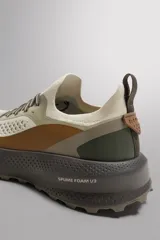 Zapatilla deportiva para hombre, color beige, con detalles en marrón y verde. Fabricada con tejido de punto transpirable y tecnología Shield Protect Max en puntera y talón. Cuenta con ajuste de cordones, tirador trasero, plantilla OrthoLite® extraíble, entresuela Spume Foam V3 y suela de goma.