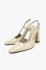 Zapato de tacón destalonado color beige acharolado, con punta fina, tacón ancho en bloque y cierre mediante tira trasera con hebilla ajustable.