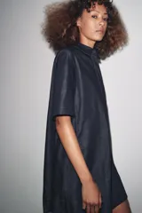 Vestido corto de Zara Woman Collection confeccionado en tejido tipo denim. Tiene cuello solapa, manga corta, bolsillos delanteros ocultos, bajo evasé y cierre frontal con botones.