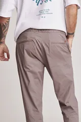 Pantalón de vestir color beige, de corte recto, con bolsillos laterales y traseros. Se ajusta a la cintura con cinturón de cuero marrón.