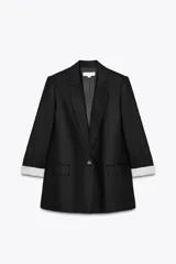 Blazer negro de lino con cuello solapa y escote pico. Manga larga con hombreras y puños con vuelta estampada a rayas. Bolsillos con solapa en el delantero, forro interior y cierre frontal con botón.
