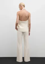 Chaleco color crema con cuello halter, espalda descubierta, botón joya, bolsillos delanteros y corte entallado.