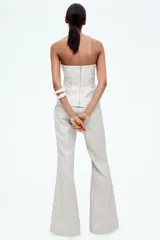 Top bustier de sarga color crudo, con escote strapless, copas acolchadas y costuras decorativas adelante y atrás. Tiene varillas delanteras para dar forma y aportar sujeción, y cierre visible en la espalda. Está forrado.