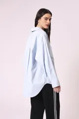 Camisa celeste de corte amplio, con cuello clásico, cierre frontal con botones y bolsillo en el pecho.