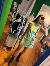 Vestido corto color verde lima con estampado floral blanco, corte cheongsam, cuello mao, sin mangas, con ribete negro y lazos decorativos en el lateral.