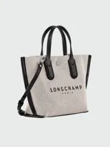 Bolso Longchamp modelo Essential Toile XS, color crudo con detalles en cuero negro. Tiene doble asa corta superior, correa larga ajustable y removible, cierre con broche a presión y logo estampado en el frente.