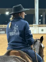 Buzo polar azul marino con cierre parcial, cuello alto y logo bordado en blanco en la espalda. La prenda es utilizada por una persona montando a caballo y usando un sombrero negro de ala ancha.