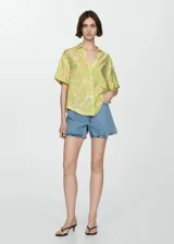 Camisa de manga corta con estampado floral en tonos verde, naranja y beige. Diseño oversize con cuello camisero y cierre frontal con botones.