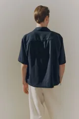 Camisa negra de manga corta en mezcla de lino y viscosa, con cuello inglés, tapeta lisa, canesú en la espalda y bajo recto. Corte holgado.