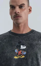 Remera negra con efecto nevado, cuello redondo y calce oversize. Estampado frontal de Mickey Mouse con una patineta.