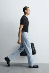 Pantalón de jean celeste de corte flare, con tiro medio, cinco bolsillos, cierre frontal con cremallera y botón, y bajo con acabado irregular.
