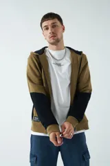 Campera marrón de felpa con capucha, cierre frontal y bolsillos laterales con cierre. Presenta mangas largas negras y logo de la marca estampado en el pecho.