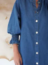 Vestido camisero corto de denim celeste, con cuello mao, mangas 3/4 con elástico en los puños y cierre frontal con botones de nácar.