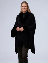 Ruana o poncho negro de tejido suave, con cuello y puños adornados con apliques de piel sintética (faux fur).