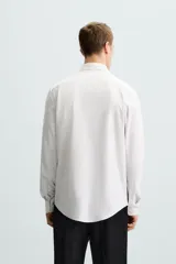 Camisa celeste a rayas verticales blancas, de corte recto, con cuello italiano abierto, mangas largas con puños abotonados y cierre frontal con botones.
