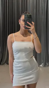 Vestido corto blanco con breteles finos, corte ajustado y frunces laterales.