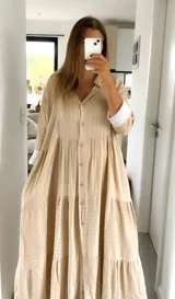 Vestido camisero largo color beige con rayas verticales blancas, cuello camisero, abotonadura frontal y mangas 3/4 con puños blancos.