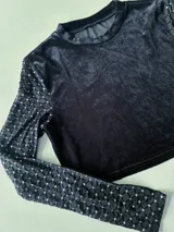 Top corto negro de terciopelo, con cuello alto y mangas largas de tul con lunares plateados.