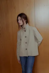 Chaqueta color beige de corte recto, cuello alto estructurado y cierre frontal con botones marrones.