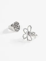 Set de dos anillos plateados de zinc. Uno con forma de flor y otro con forma de sello circular con textura machacada.
