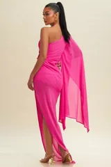 Vestido largo de fiesta fucsia, con un solo hombro y manga larga tipo capa. Tiene un corte ajustado con drapeado en la cintura y abertura lateral en la falda.