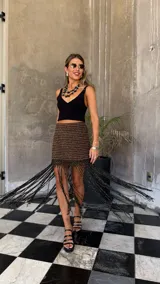 Falda corta tejida a mano en crochet, con diseño a rayas horizontales en tonos marrón oscuro y dorado brillante. Presenta un borde inferior con flecos largos y abundantes.