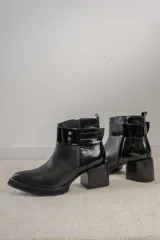 Bota corta de cuero marrón con puntera redondeada y taco cuadrado. Presenta una correa con hebilla alrededor del tobillo y cierre lateral.