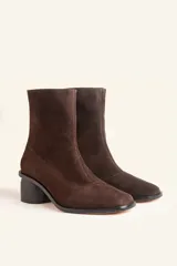 Bota corta de cuero vacuno color marrón oscuro, con diseño sin forro y taco cilíndrico de madera tallada a mano. Presenta cierre posterior y punta redondeada.