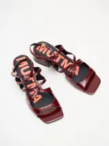 Sandalias de cuero charol color borgoña con tiras finas, taco cuadrado bajo y cierre con hebilla en el tobillo. Interior con estampado del logo de la marca en color naranja.