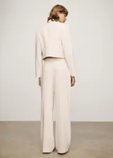 Pantalón de tiro medio color crema a rayas verticales finas, con dos bolsillos delanteros, cierre oculto de botón, gancho y cremallera, diseño recto y largo.