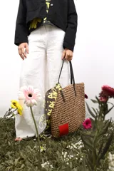 Bolso de rafia color beige con asas de cuero marrón y parche de cuero rojo en una esquina.