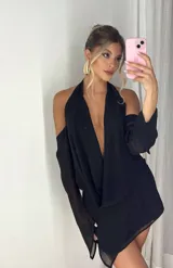 Vestido corto negro con escote pronunciado en V y drapeado en el busto. Presenta mangas largas con aberturas en los hombros (cold shoulder) y puños acampanados.