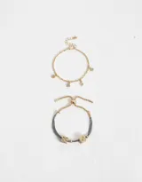 Set de dos pulseras doradas, una con cadena y dijes colgantes de strass con forma de trébol, corazón, rombo y flor. La otra pulsera es de hilo de lurex gris con cadena dorada y dijes de dados dorados.