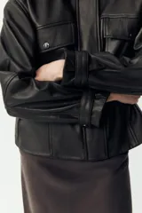 Cazadora negra de cuero con cuello solapa, manga larga con trabilla y bolsillos de parche con solapa en el delantero. Cierre frontal con cremallera y botones a presión ocultos por solapa.
