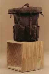 Mochila marrón de lona con detalles en cuero, cierre superior enrollable con hebillas y dos bolsillos frontales con hebilla.