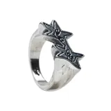 Anillo de metal plateado con diseño de dos estrellas superpuestas con detalles grabados en relieve que simulan un rayo o un trazo artístico.