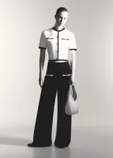 Pantalón negro de punto fino con diseño recto y largo, tiro medio, cintura elástica, ribetes en contraste y bolsillos de ribete delanteros con botones decorativos.
