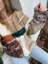 Sweater de punto grueso con diseño patchwork en tonos neutros, verde y naranja.