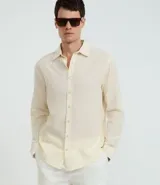 Camisa de hombre de manga larga, color crema o blanco roto, con cuello camisero y abotonadura frontal.