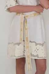 Vestido corto color blanco, confeccionado en lino con detalle de flores aplicadas en el ruedo, mangas y cuello. Incluye lazo a tono para ajustar en la cintura.